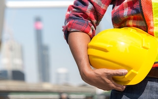 Architect worker holding yellow helmet a for workers security control at city site.
